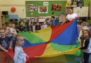 Dzieci z gr. II bawią się chustą animacyjną podczas wspólnych zabaw z panią z kuchni