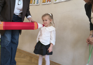 Pani Dyrektor pasuje dziewczynkę na przedszkolaka, dużą czerwoną kredką